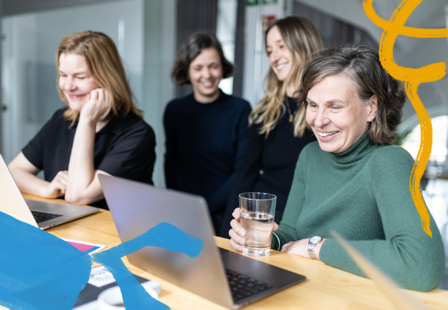 Das Team von bcause, zwei Personen sitzen vor ihren Laptops, zwei stehen lächelnd dahinter.